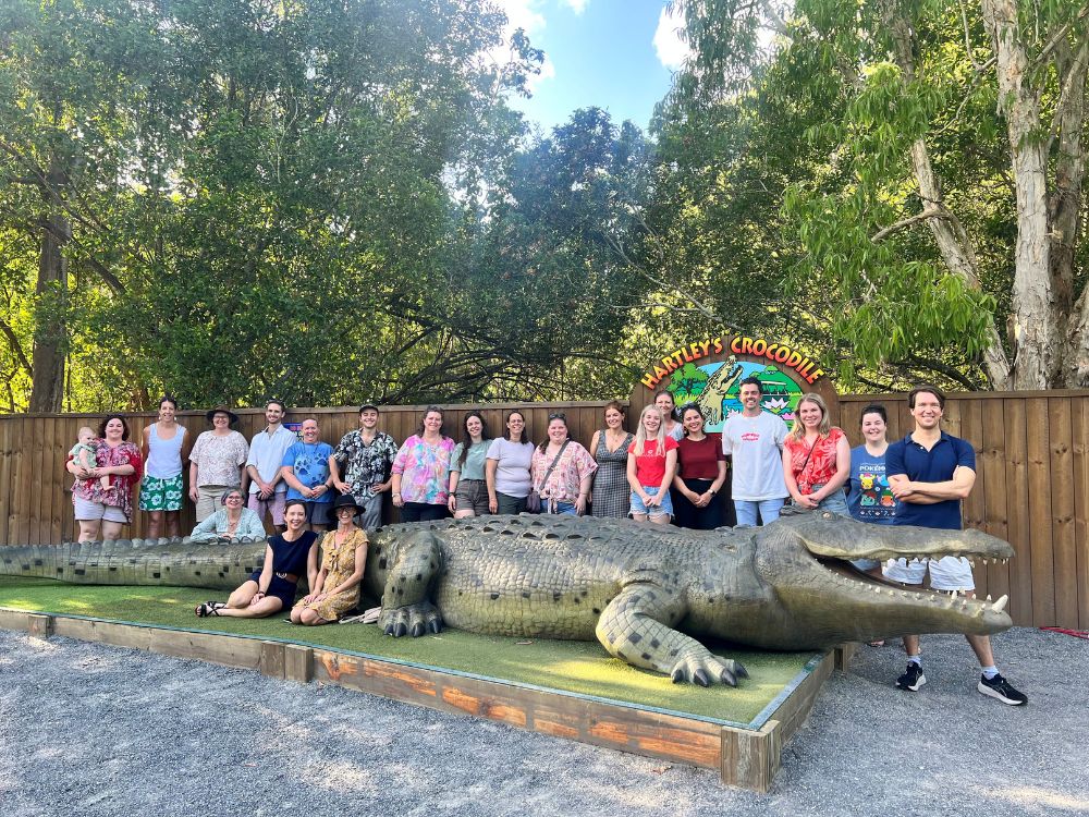 a group of people posing in front of a fake crocodile